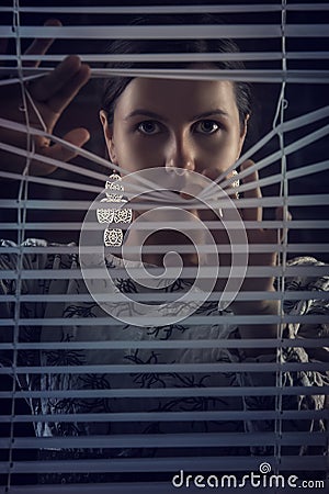 Portrait of beautiful mysterious woman looking through jalousie,louver Stock Photo