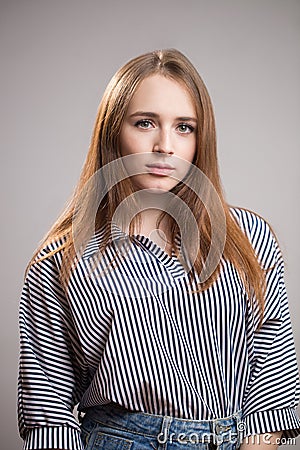 Portrait of a beautiful redhead woman wearing a striped blouse and looking at the camera on a gray background. Young student girl Stock Photo