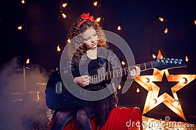 Portrait of a Beautiful rock girl with curly hair wearing leather jacket, boots playing the electric guitar while Stock Photo