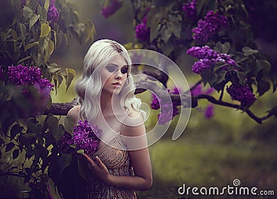 Portrait of a beautiful sensual young blond woman in spring. Blossoming spring garden. Young girl in a gold dress Stock Photo