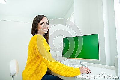 Portrait of a beautiful smiling woman, working at the computer with green screen, in an office environment Stock Photo