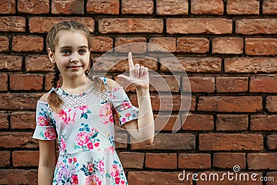 Portrait of a beautiful teenage girl, against a brick wall, the girl raises her finger up, points to an object Stock Photo