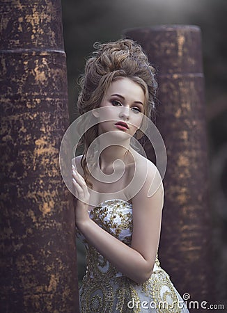 Beautiful woman in an ancient medieval dress, with a high complex historical hairstyle near the walls of the castle. Stock Photo