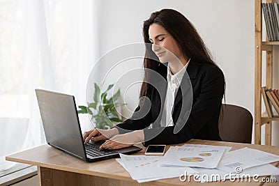 Portrait of a beautiful woman data analyst sitting at a desk working on a laptop. Stylish woman in an office setting Stock Photo