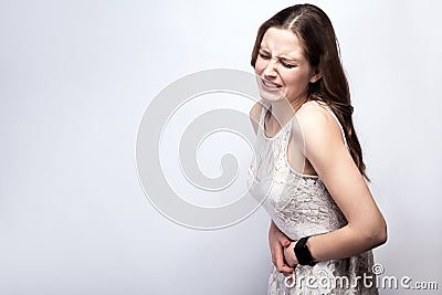 Portrait of beautiful woman with freckles and white dress and smart watch with stomach pain on silver gray background. Stock Photo