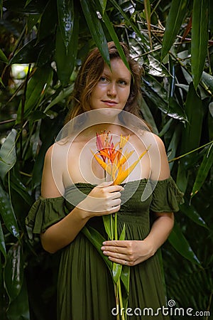 Portrait of beautiful woman with heliconia flowers in jungle. Caucasian woman in tropical rain forest, wearing green dress. Nature Stock Photo