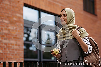 Beautiful woman in hijab standing on city street. Muslim studnet eating apple, going to school. Iran, Afganistan female Stock Photo