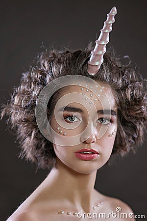 Portrait of a beautiful woman with a make-up and beads on her face , pink horn , unicorn , fashion photo shoot Stock Photo