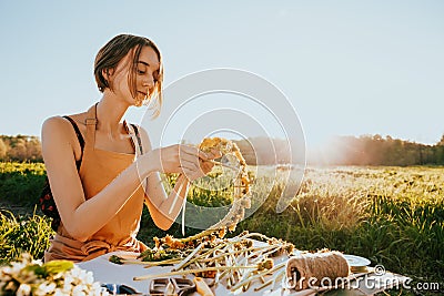 Portrait of beautiful woman making wreath of flowers dandelions on flowering field. Summer lifestyle, nature lover and freedom Stock Photo