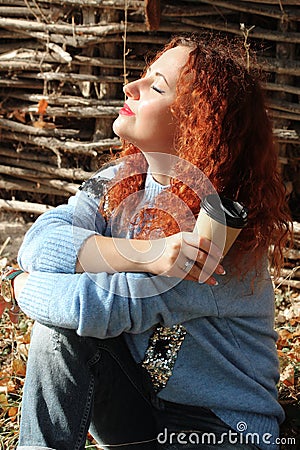 Portrait of a beautiful woman with red hair sitting on the grass with eyes closed from behind the sun Stock Photo