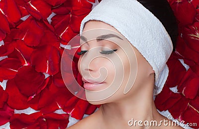 Portrait of a beautiful woman in a spa salon in front of a beauty treatment against the background of red rose petals. Stock Photo