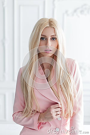 Portrait of a beautiful young blonde woman in a pink stylish jacket stands in a white bright room. Stock Photo