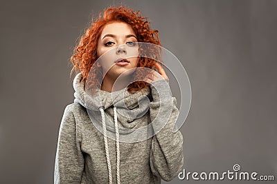 Portrait of a beautiful young curly-haired girl with fiery red hair looking at the camera on a gray background. Stock Photo