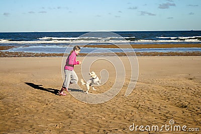 Portrait of a beautiful young girl and her puppy running on the beach Stock Photo