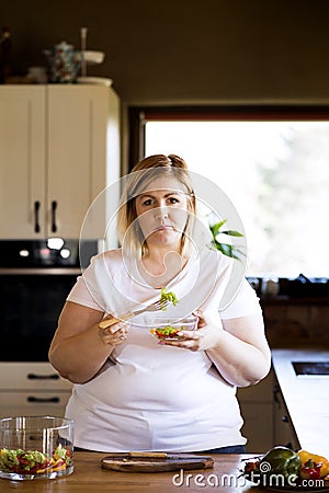 Portrait of beautiful young overweight woman choosing healthy food, eating vegetable salad. Beauty and body positivity Stock Photo