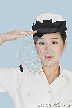 Portrait of a beautiful young US Navy officer saluting over light blue background Stock Photo