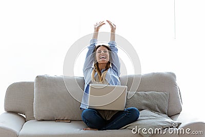 Beautiful young woman celebrating a succes while working with laptop at home. Stock Photo