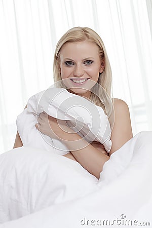 Portrait of beautiful young woman covering herself with bedsheet in bed Stock Photo