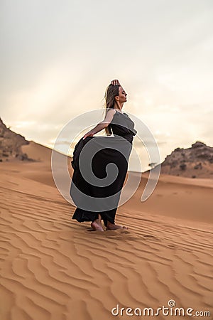 Portrait of beautiful young woman in long fluttering black dress posing outdoor at sandy desert Stock Photo