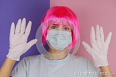 Portrait of beautiful young woman with pink hair wearing medical mask and medical latex gloves on a pink and violet background Stock Photo