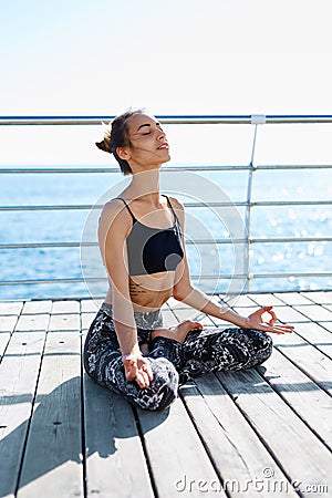 Portrait of a beautiful young woman sitting in lotus pose at the beach with sea background. Feeling so comfortable and Stock Photo