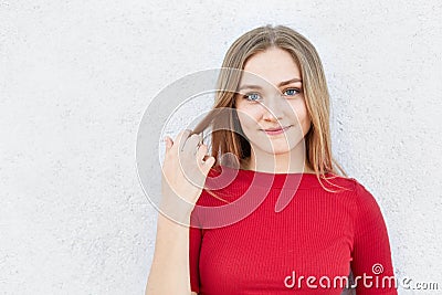 Portrait of beautiful young woman with straight blonde hair, alluring eyes and thick lips having pleased expression while looking Stock Photo