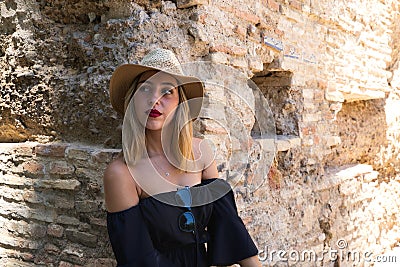Portrait of a beautiful young woman wearing a hat and sunglasses against the backdrop of a ruined building. The woman`s lips are Stock Photo