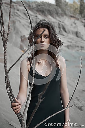 Portrait of a beauty fashion woman in the branches of a dead tree. Girl on the background of sand mountains Stock Photo