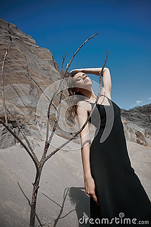 Portrait of a beauty fashion woman in the branches of a dead tree. Girl on the background of sand mountains Stock Photo