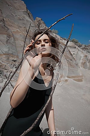 Portrait of a beauty fashion woman in the branches of a dead tree. Girl on the background of sand mountains Stock Photo