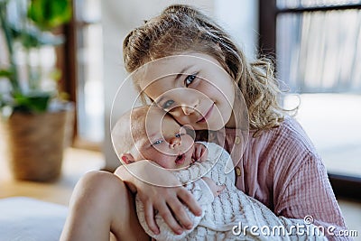 Portrait of big sister holding newborn sister. Girl carefully cuddling small baby. Sisterly love, joy for new family Stock Photo