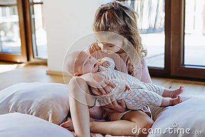 Portrait of big sister holding newborn sister. Girl carefully cuddling small baby. Sisterly love, joy for new family Stock Photo