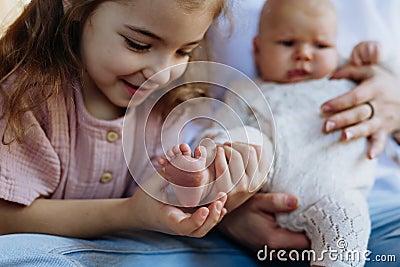 Portrait of big sister kooking at small foot of little baby. Sisterly love, joy for new family member. Stock Photo