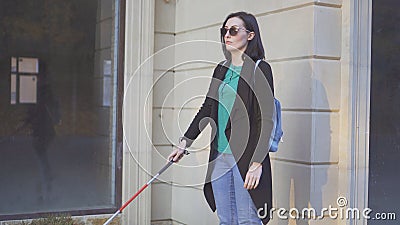 A blind woman wearing glasses with a cane walking in front of shop windows Stock Photo