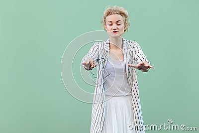 Portrait of blind young blonde woman in white shirt, skirt, and striped blouse standing, with closed eyes and trying to touch or Stock Photo