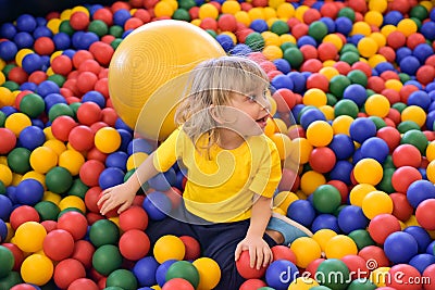 Portrait of a blond boy in a yellow t-shirt. The child smiles and plays in the children`s playroom. Ball pool Stock Photo