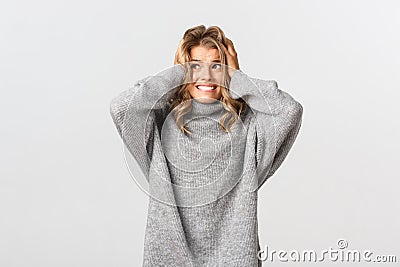 Portrait of blond girl in panic, looking left and holding hands on head, feeling alarmed and distressed, standing over Stock Photo
