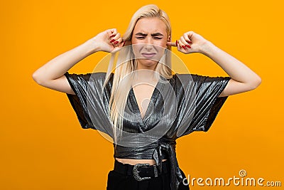 Portrait of a blond lady showing discontent covering her ears with her hands and squinting on a yellow studio background Stock Photo