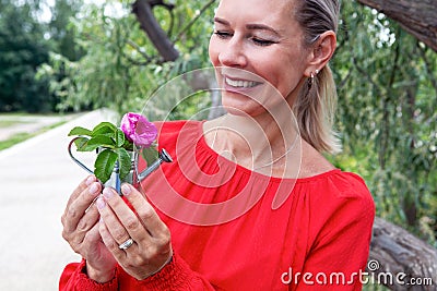 Blond woman outdoors holding a miniature watering can with a flower Stock Photo