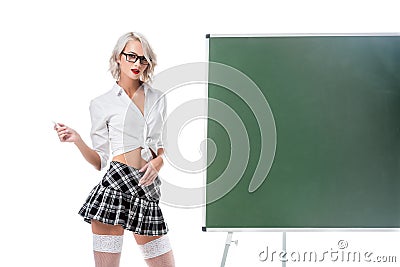 portrait of blond woman in seductive school uniform with piece of chalk standing at empty chalkboard Stock Photo