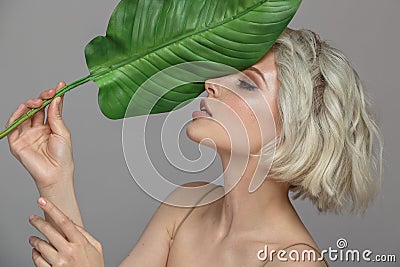 Portrait of blonde woman and green leaf. Organic cosmetics concept. Stock Photo