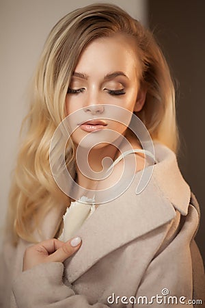 Portrait of a blonde woman wearing beige coat, looking over shoulder. Stock Photo