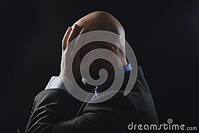 Portrait of a bold male man in dark suit hands at head, Pain concept. Bodyguard at work. Dark dramatic background Stock Photo