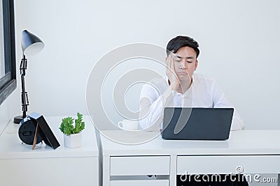 Portrait of bored Asian young handsome businessman wear white shirt working with laptop at office. Unmotivated employee Stock Photo