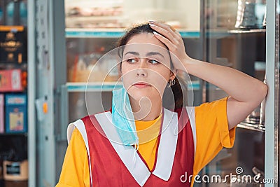 Portrait of a bored employee in uniform, with a medical mask over his ear. Showcase with products in the background. Concept of Stock Photo