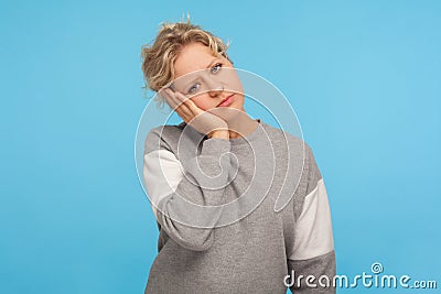 Portrait of bored exhausted woman with short curly hair in sweatshirt leaning on hand and looking at camera with disinterest Stock Photo