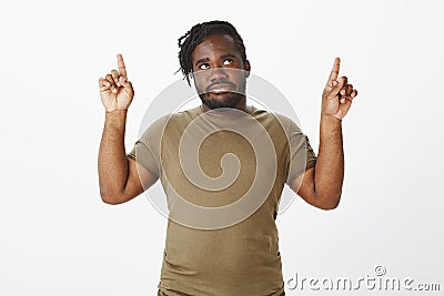 Portrait of bothered displeased african bearded man in military clothes, raising index fingers, looking and pointing up Stock Photo