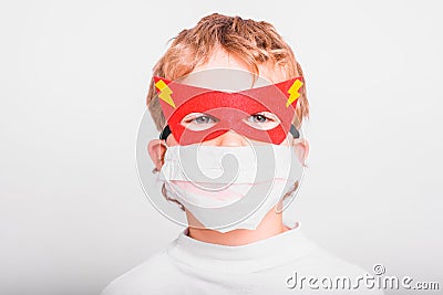 Portrait of boy in superhero mask with his mouth covered with a medical mask to protect himself from viral infections and diseases Stock Photo