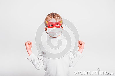 Portrait of boy in superhero mask with his mouth covered with a medical mask to protect himself from viral infections and diseases Stock Photo