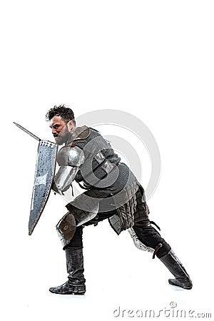 Portrait of brave medieval warrior, knight in special armor protecting himself with shield and sword isolated over white Stock Photo